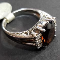 Vintage sterling silver ring with. Center CZ is deep brown (Smoky Quartz color) measuring 11x10mm, with three clear CZs on each side in an engagement ring style. The Euro band has intricate cutout scrollwork with beautiful craftsmanship. The ring shank is 2.5mm wide at the back. If you love finding unique treasures, then a vintage ring may be just the thing to add to your collection. Our family acquired this ring around 2000, as part of a large jewelry collection. It's in great condition, unworn Brown Diamond Ring With Accents For Anniversary, Brown Diamond Ring With Diamond Accents For Anniversary, Classic Oval Brown Ring, Brown Diamond Jewelry For Formal Occasions, Classic Brown Oval Ring, Anniversary Brown Diamond Ring With Accents, Formal Brown Diamond Jewelry, Brown Rings With Prong Setting For Anniversary, Brown Prong-set Ring For Anniversary