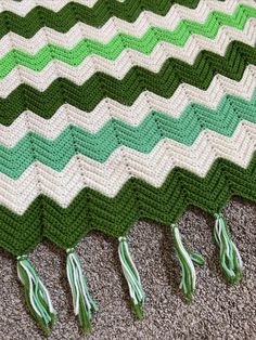 a crocheted blanket with tassels on the bottom and green trim around it