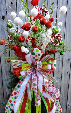 a christmas wreath with red, white and green ornaments hanging on the side of a wooden fence