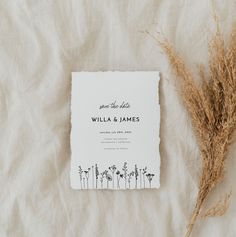 a wedding save - the - date card and some dried grass on a white sheet