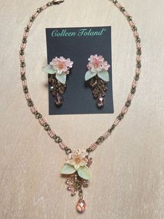 Colleen Toland Fairy Pink Flower Pendant Set.   Fairy Pink flower pendant necklace with lovely soft peach colored flowers surrounded with hand painted green leaves and a single pink fire-polish drop.  The necklace is made with delicate pink seed beads and linked together with gold colored jump-rings.  The closure is a lobster claw with a 4 inch extender so as the length can be adjusted. The earrings are made with the same lovey pink flowers and leaves and are finished with pink drop beads. Earrings and Necklaces sold separately or as a set. This is a quality piece of jewelry that will last a life time. Created by designer Colleen Toland who has been creating her unique style of vintage jewelry for more than 30 years. All of our pieces come with an engraved tag with Colleen's name so as you Handmade Flower-shaped Rose Gold Jewelry, Handmade Flower Shaped Rose Gold Jewelry, Adjustable Peach Jewelry For Gifts, Elegant Handmade Rose Gold Beaded Necklaces, Handmade Pink Pendant Flower Necklace, Whimsical Flower Jewelry For Jewelry Making, Adjustable Pink Jewelry With Handmade Flowers, Delicate Handmade Dangle Jewelry With Flowers, Delicate Handmade Flower Dangle Jewelry