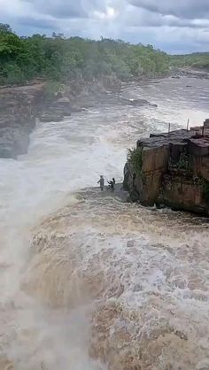 two people standing on the edge of a cliff in water with waves crashing over it