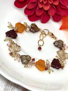 This gorgeously unique bracelet features beautifully detailed Czech glass leaves in crisp autumn hues. Rich colors of olive green, golden crystal, warm pumpkin orange, and deep berry burgundy wrapped in 14k yellow gold filled dance along this extraordinary piece. Petite clusters of peridot, garnet, peach freshwater pearls and rainbow Austrian Crystal are nestled between each tender leaf. Finished with a generously-sized 14k yellow gold filled lobster claw clasp and polished, oval link extender chain. A plump, deep berry red garnet charm completes this piece. Arrives in a lovely box, ready for giving or safekeeping. -Adjustable to fit most wrist sizes  -All metal components are 14k yellow gold filled. NOT gold plated. Gold filled is required by law to contain a certain percentage of real go Fall Jewelry Trends, Golden Crystal, Cluster Bracelet, Crisp Autumn, Cluster Bracelets, Rose Quartz Earrings, Pumpkin Earrings, Autumn Leaf, Leaf Jewelry