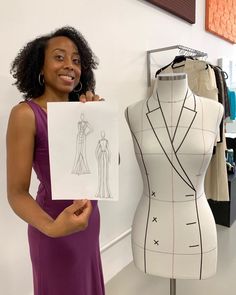 a woman standing next to a mannequin holding up a piece of paper with a drawing of a dress on it