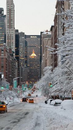 a city street covered in snow and surrounded by tall buildings with cars driving down it