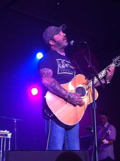 a man that is standing up with a guitar in front of some microphone's