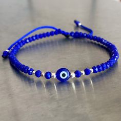 Adjustable Evil eye bracelet crafted by hand from 100% blue nylon string. Description: *3mm  Blue crystal *3, 2 and 1mm silver beads *Blue glass evil eye Size: Adjustable from 6" to 8" The bracelet opens by pulling the beads closest to the sliding knot in opposite directions and closes by pulling the small, dangling blue beads in opposite directions. Cheap Blue Evil Eye Bracelet For Friendship, Adjustable Blue Evil Eye Bracelet, Blue Adjustable Evil Eye Bracelet, Adjustable Blue Evil Eye Bracelet For Spiritual Purposes, Adjustable Blue Spiritual Evil Eye Bracelet, Blue Spiritual Friendship Bracelets With Sliding Knot, Blue Spiritual Friendship Bracelet With Sliding Knot, Adjustable Blue Evil Eye Bracelet Hand-strung, Adjustable Blue Evil Eye Bracelet With Sliding Knot