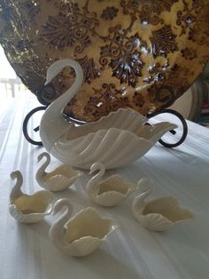 two white swans sitting on top of a table next to a large bowl and vase