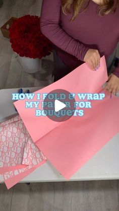 a woman cutting out pink paper on top of a table