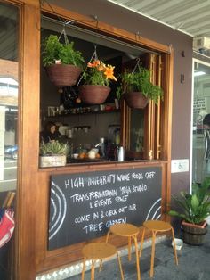 an outdoor cafe with potted plants in the window and sign on the front door