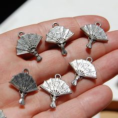 a person is holding some silver charms in their hand and it looks like they have fan shaped designs on them