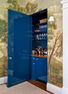 a blue cabinet with wine glasses on it in a room that is decorated with wallpaper