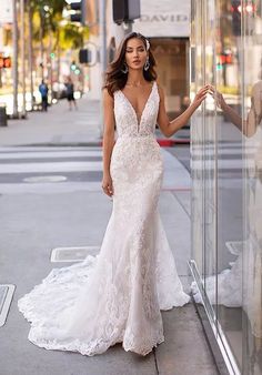 a woman in a wedding dress leaning against a glass wall on the side of the street