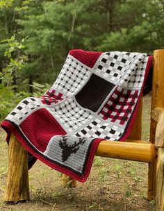 a red and white crocheted blanket sitting on top of a wooden bench in the woods