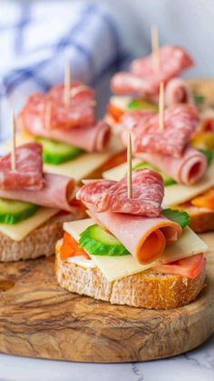 small sandwiches with meats and cheese are on a cutting board, ready to be served