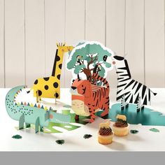 some cupcakes are sitting on a table next to paper cut out animals and giraffes