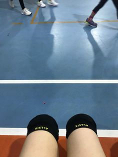 the legs and ankles of people in sports shoes on a blue floor with yellow lines