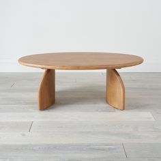 an oval wooden table with curved legs on a wood floor in front of a white wall