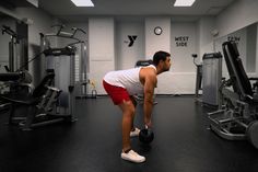 a man lifting a kettle in a gym with other machines and exercise equipment behind him