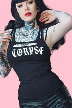 a woman with black hair and tattoos on her chest wearing a shirt that says corpse