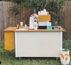 an outdoor bar is set up outside in the grass with flowers and bottles on it