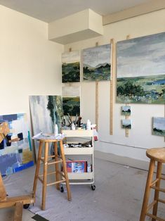 an artist's studio with several paintings on the wall and two wooden stools