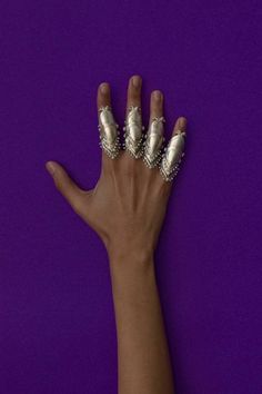 a woman's hand with two silver rings on top of her fingers against a purple background