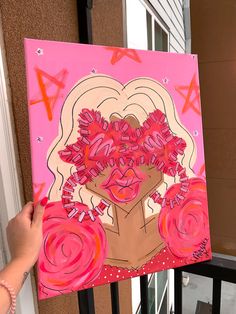 a person holding up a painting with pink flowers on it in front of a window