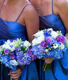 three bridesmaids in blue dresses holding bouquets of purple and white flowers together