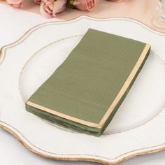 a green book sitting on top of a white plate next to flowers and a glass