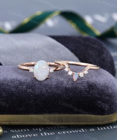 an opal and diamond ring sits on top of a velvet cushion next to a ribbon