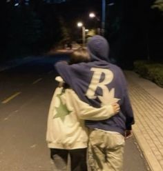 two people walking down the street at night with their arms around each other and one person wearing a hoodie