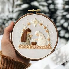 a person holding up a cross stitch christmas ornament with a nativity scene on it