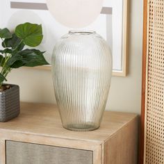 a white vase sitting on top of a wooden table next to a plant in a pot