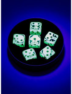 glow in the dark dices on a black plate with blue light behind them and skull designs