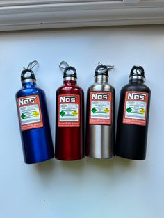 three stainless steel water bottles are lined up against a white wall, one is red and the other two are blue