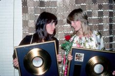 two women standing next to each other holding gold and black records with roses in them