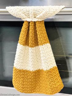 a yellow and white crocheted dish towel hanging from the handle of an oven