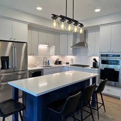 a kitchen with white cabinets and blue counter tops, black chairs and an island in the middle