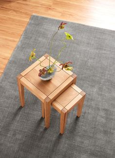 two wooden tables sitting on top of a gray rug next to a planter filled with flowers