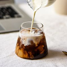 a person pouring milk into a glass on a table with a laptop in the background