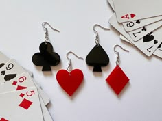 four playing cards and three pairs of earrings on a white surface with ace's, spades and hearts