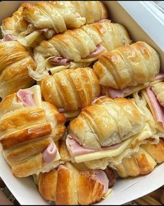 several croissants with ham and cheese in a white box on a table