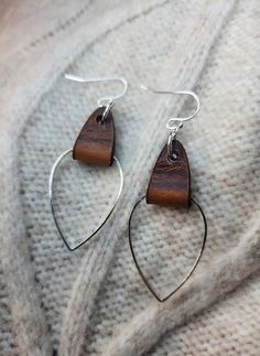 the earrings are made out of wood and silver wire, which is hanging on a white sweater