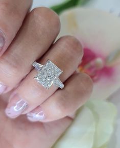 a close up of a person's hand with a ring on their finger and a flower in the background