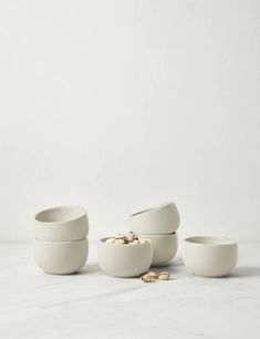 three white bowls with gold coins in them on a marble countertop next to each other