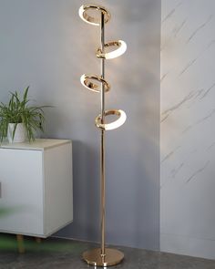 a modern floor lamp with three lights on each side and a plant in the corner