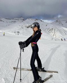 a woman on skis in the snow with other skiers and mountains behind her