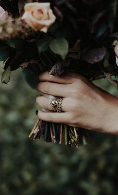 a person holding a bouquet of flowers with two wedding rings on their fingers and the other hand