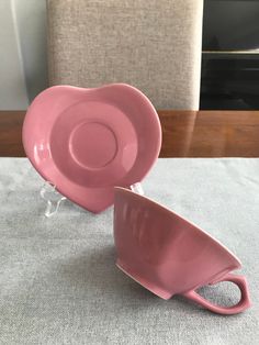 two pink cups and saucers sitting on a gray tablecloth with a chair in the background